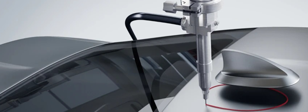 A robotic arm applies adhesive to a car windscreen, preparing it for installation on an assembly line.